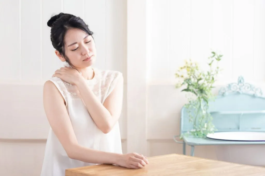 右肩に左手を当てる女性