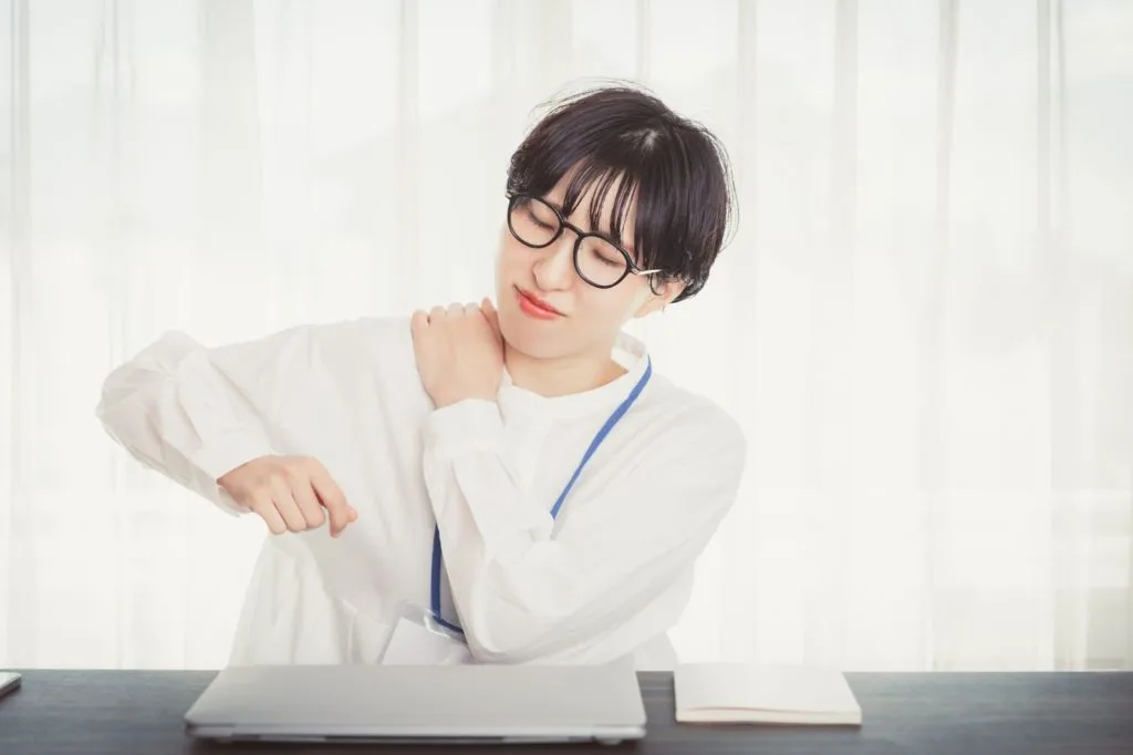 首が凝って左手で右肩を押さえる様子