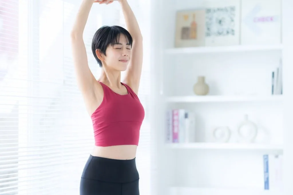 両手を上で組んで伸びをする女性