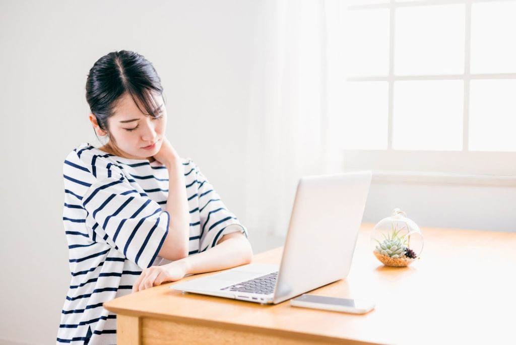 デスクワークをしながら首凝りを気にする女性