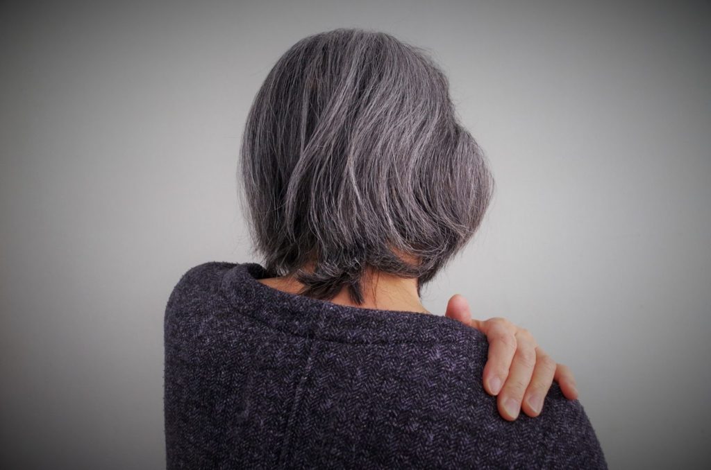 左手で右肩を押さえる白髪の女性