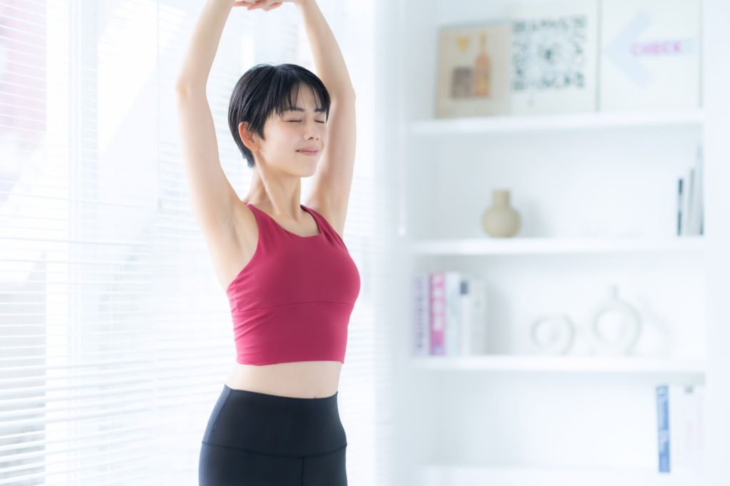両手を上で組んで伸びをする女性